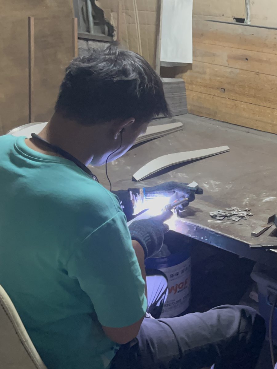 Worker welding a tubular metal chair frame at a workshop bench